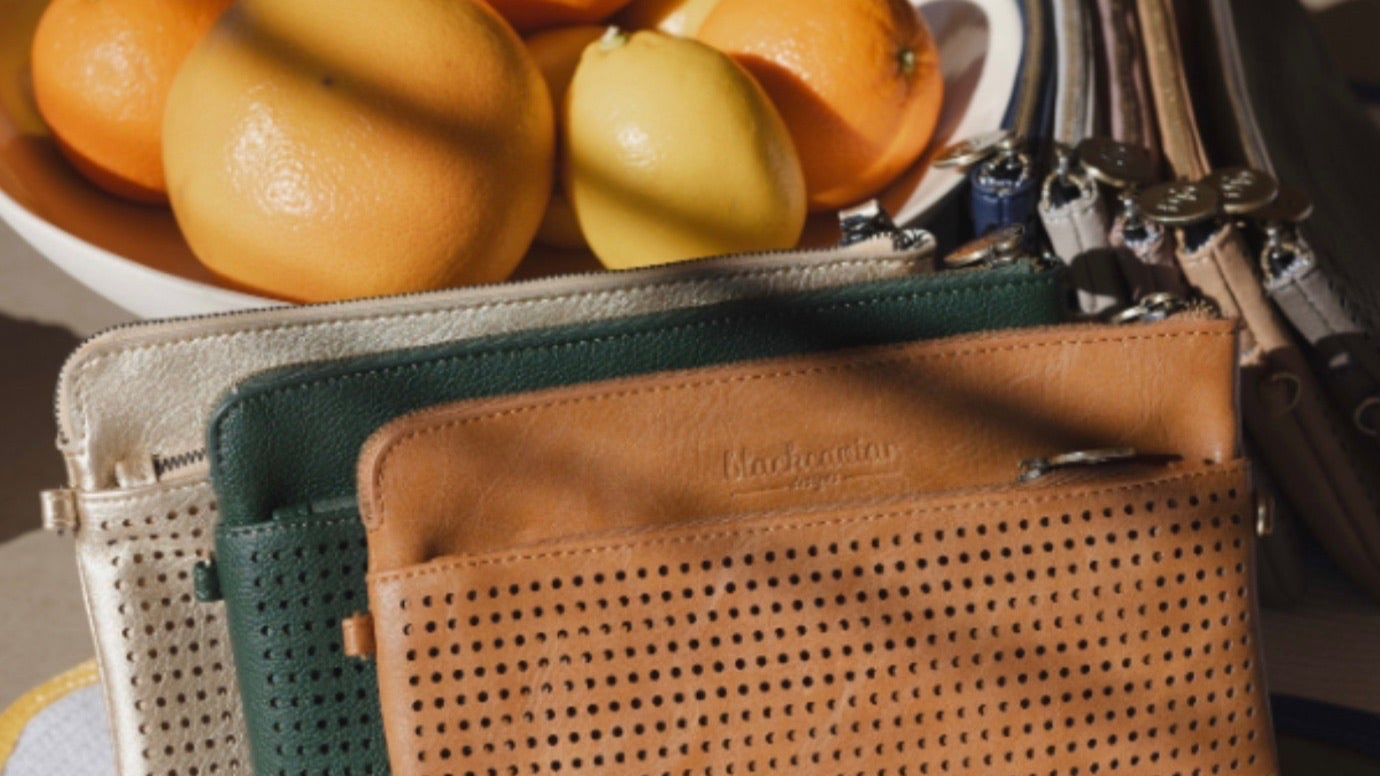 Selection of leather handbags next to a bowl of oranges